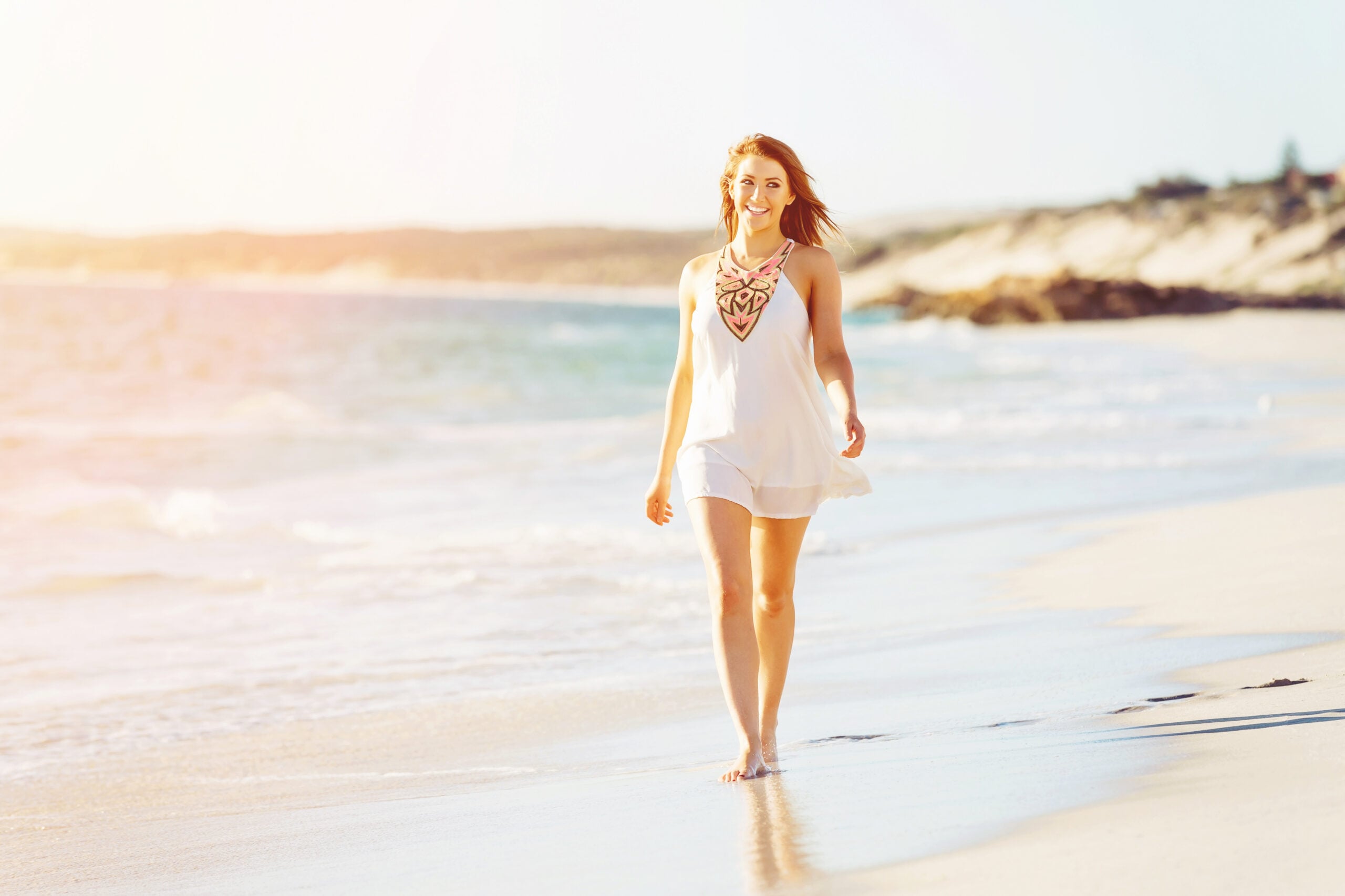 Woman walking along the shoreline in bright sunlight